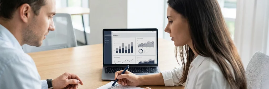 Zwei Personen besprechen im Meeting Kennzahlen aus einem Analytics-Dashboard und einem Ausdruck – Grundlage für e-commerce Strategieberatung.