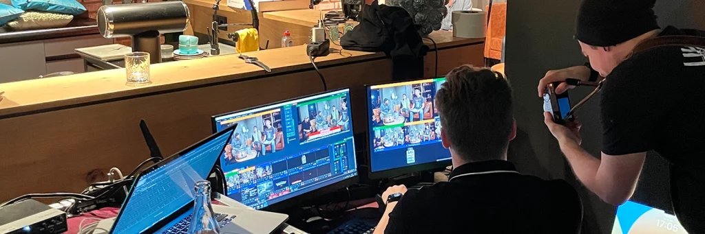 Zwei Personen sitzen an einem Regieplatz mit mehreren Monitoren, auf denen das YouTube-Live-Set in verschiedenen Kameraperspektiven zu sehen ist – technische Steuerung des Markenerlebnisses.