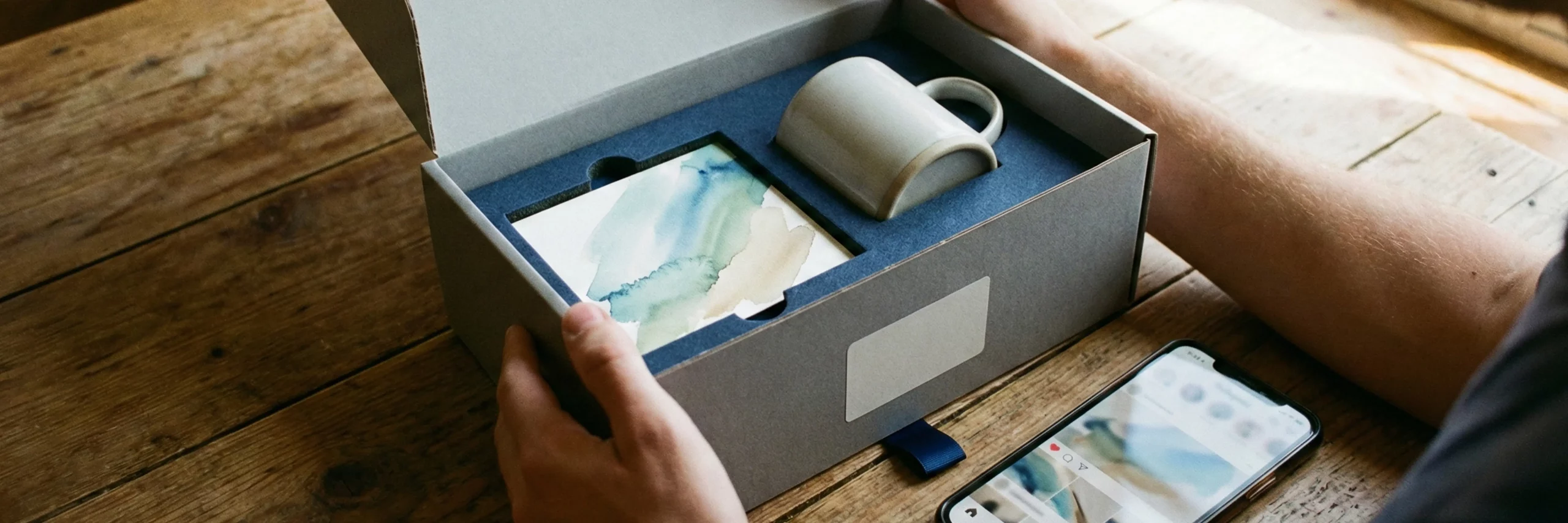 Person öffnet eine sorgfältig verpackte Bestellung mit Produkt, Inlay und Karte; das Paket zeigt Fulfillment als Markenerlebnis, das Markenbekanntheit stärkt.