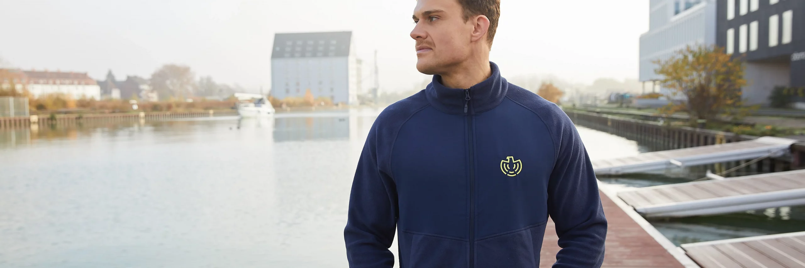 Ein Mann trägt eine offizielle blaue Jacke aus dem BND Online Shop vor einer maritimen Kulisse.
