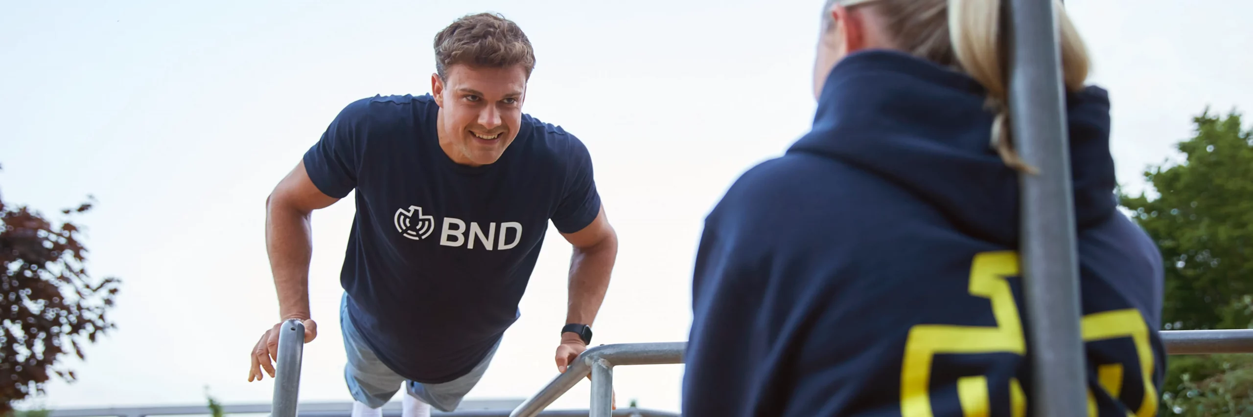 Ein sportlicher Mann in einem T-Shirt aus dem BND Online Shop macht Liegestütze im Freien.